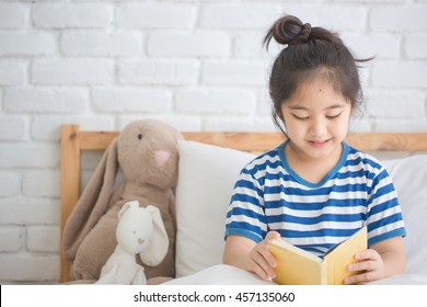 Happy Asian Girl Reading Story Book On The Bed