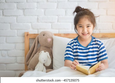 Happy Asian Girl Reading Story Book On The Bed