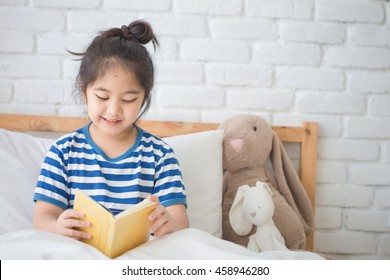 Happy Asian Girl Reading Story Book On The Bed