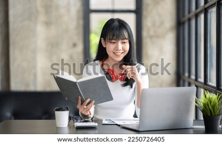 Happy Asian girl student wear wireless headphone study online with the teacher, happy young woman learn language listen lecture watch webinar write notes look at laptop sit in cafe, distance education