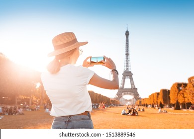 Happy Asian girl takes photo on her smartphone on the background of the Eiffel tower. Travel and image quality concept