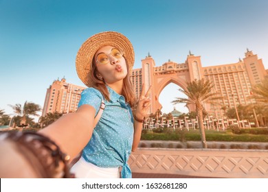 Happy asian girl traveller taking selfie photo with the famous luxury Atlantis hotel building on a Jumeirah Palm Island in Dubai, UAE. Vacation and tourist destination concept