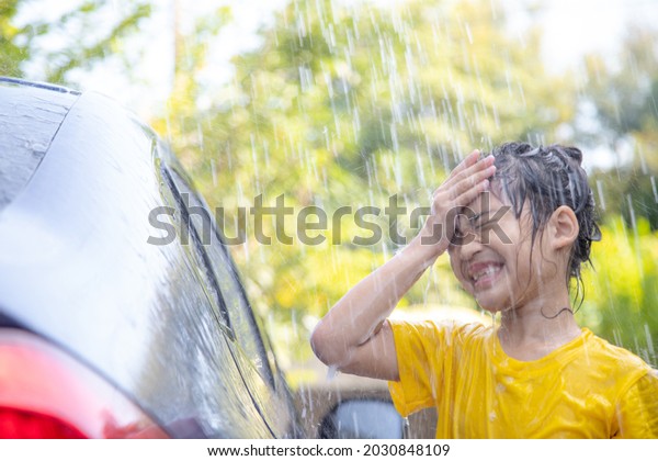 Happy Asian girl washing car on water splashing and\
sunlight at home