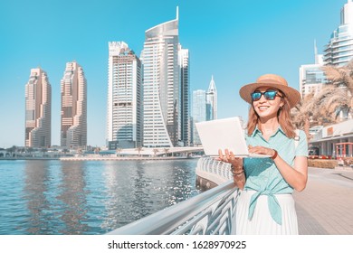 Happy asian girl works at a laptop in Dubai Marina port against the backdrop of high skyscrapers and the Bay