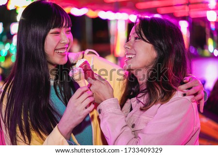 Happy asian girls eating candy sweets ice cream at amusement park - Young trendy friends having fun together- Tech, friendship and millennial generation concept - Focus on faces