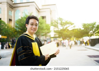 Happy Asian Graduate Student Holding The Diplomas On Hand During The University Graduation Ceremony. Master Degree Student In Gown Suit Holding A Diplomas For Photography.