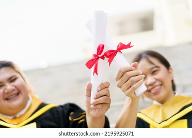 Happy Asian Graduate Student Holding The Diplomas On Hand During The University Graduation Ceremony. Master Degree Student In Gown Suit Holding A Diplomas For Photography.