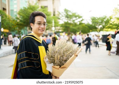 Happy Asian Graduate Student Holding A Beautiful Bouquet Of Flowers In The University Graduation Ceremony. Master Degree Student In Gown Suit Showing A Bouquet Of Flower For Photography.