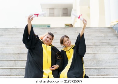 Happy Asian Graduate Student Holding The Diplomas On Hand During The University Graduation Ceremony. Master Degree Student In Gown Suit Holding A Diplomas For Photography.