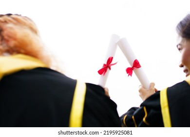 Happy Asian Graduate Student Holding The Diplomas On Hand During The University Graduation Ceremony. Master Degree Student In Gown Suit Holding A Diplomas For Photography.