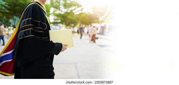 Happy Asian Graduate Student Holding The Diplomas On Hand During The University Graduation Ceremony. Master Degree Student In Gown Suit Holding A Diplomas For Photography.