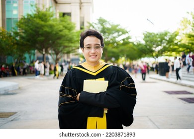 Happy Asian Graduate Student Holding The Diplomas On Hand During The University Graduation Ceremony. Master Degree Student In Gown Suit Holding A Diplomas For Photography.