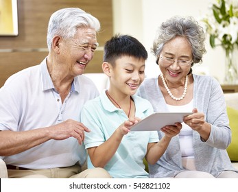 Happy Asian Grandfather And Grandmother Looking At Tablet Computer With Grandson, Happy And Smiling.