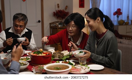 happy asian grandmother and daughter in law giving food to each other while eating dinner together on the eve of Chinese new year at a cozy home interior.