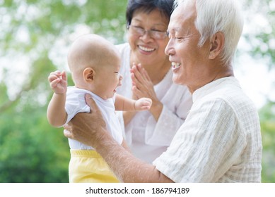 Happy Asian Grandparents Playing With Baby Grandchild At Outdoor Garden.