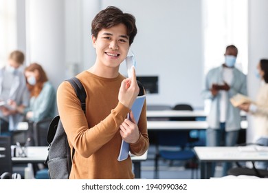 Happy Asian Guy Taking Off Disposable Medical Mask At Classroom