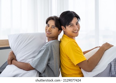 Happy Asian Homosexual Gay Couple Sitting On Bed Back To Back Against Other, LGBT Concept. Looking At Camera.