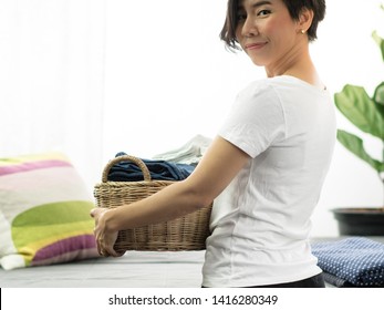 A Happy Asian Housewife Carry A Weaving Bamboo Laundry Basket Full Of Clean Folded Cloths And Towels. Woman Daily Household Chores, Wife, Mom Routine Housework Concept.