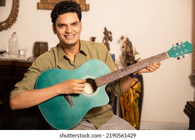 Happy Asian Indian Young Man Playing Acoustic Guitar At Home, Music Teacher Or Male Musician.