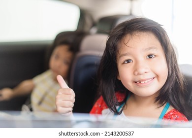 Happy Asian Kid Tween Girl Thumb Up With Smile On Seat.Family Riding Car Traveling By Automobile. Asian Family Parenting And Children Enjoying Summer Road Trip Together.Sibling Kids On Car Fun Trip.