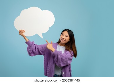 Happy asian lady pointing at empty speech bubble, smiling at camera on blue studio background, mockup. Excited female teenager with blank word cloud, space for text. News, dialog, announcement