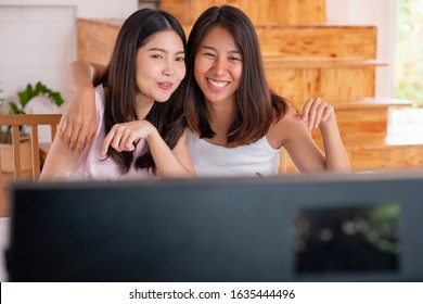 Happy Asian Lesbian Couple Watching Television While Eating Breakfast At Kitchent In Cozy Home