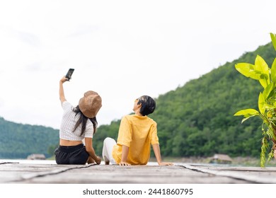 Happy Asian LGBTQ couple using mobile phone taking selfie together on lake house balcony. People enjoy and fun outdoor lifestyle travel nature forest mountain and ocean on summer holiday vacation. - Powered by Shutterstock