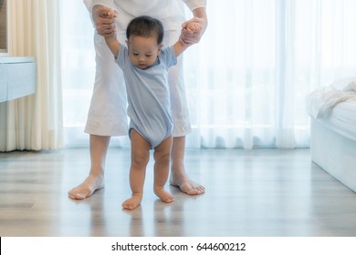 Happy Asian Little Baby Boy Learning To Walk With Mother Help In Bedroom At Home. Family, Child, Childhood And Parenthood Concept