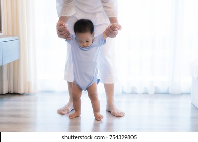 Happy Asian Little Baby Boy Learning To Walk With Mother Help In Bedroom At Home. Family, Child, Childhood And Parenthood Concept