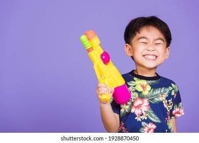 Happy Asian Little Boy Holding Plastic Water Gun, Thai Kid Funny Hold Toy Water Pistol And Smiling, Studio Shot Isolated On Purple Background, Thailand Songkran Festival Day National Culture Party