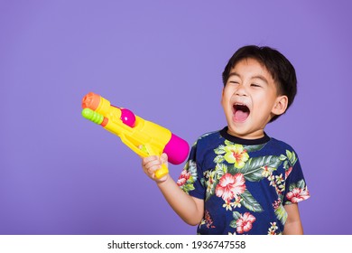 Happy Asian Little Boy Holding Plastic Water Gun, Thai Kid Funny Hold Toy Water Pistol And Smiling, Studio Shot Isolated On Purple Background, Thailand Songkran Festival Day National Culture Party