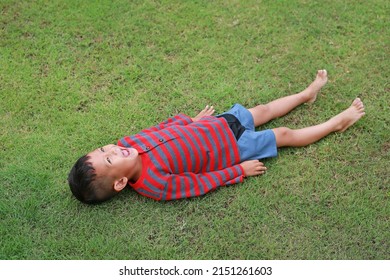 Happy Asian Little Boy Lying Down On Green Lawn. Kid Lies On Grass Looking On Sky.