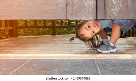 Happy Asian Little Child Girl Plays Peekaboo Under The Wooden Door In The Garden.