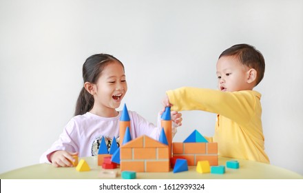Happy asian little child girl and baby boy playing a colorful wood block toy on table over white background. Sister and her brother playing together.