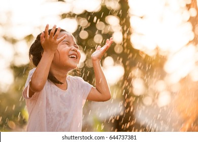 Happy asian little child girl having fun to play with the rain in the evening sunlight in vintage color tone