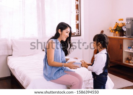 Happy asian little daughter with mother holding gift box together at home