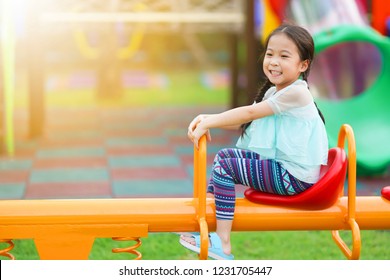 Happy Asian Little Girl Playing On Teetering Board In Playground. Kid Play See Saw        