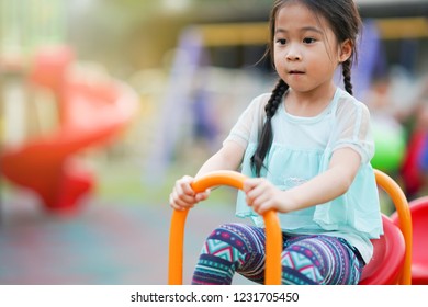 Happy Asian Little Girl Playing On Teetering Board In Playground. Kid Play See Saw        