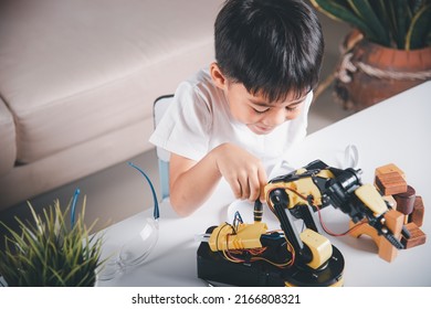 Happy Asian Little Kid Boy Using Screwdriver To Fixes Screws Robotic Machine Arm In Home Workshop, Child Learning Repairing Get Lesson Control Robot Arm, Technology Future Science Education Concept