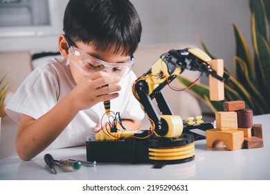 Happy Asian Little Kid Boy Using Screwdriver To Fixes Screws Robotic Machine Arm In Home Workshop, Child Learning Repairing Get Lesson Control Robot Arm, Technology Future Science Education Concept