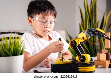 Happy Asian Little Kid Boy Using Screwdriver To Fixes Screws Robotic Machine Arm In Home Workshop, Child Learning Repairing Get Lesson Control Robot Arm, Technology Future Science Education Concept