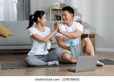 Happy asian lovers celebrating success after morning workout, using laptop, cheerful man and woman in sportswear sitting on yoga mat, holding bottles with water, giving each other high five, smiling - Powered by Shutterstock