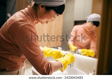 A happy asian maid is cleaning sink in bathroom at home.