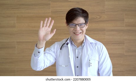 Happy Asian Male Doctor Waving A Hand And Smiling To Camera. 