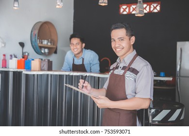 Happy Asian Male Waiter In Apron Writing Order