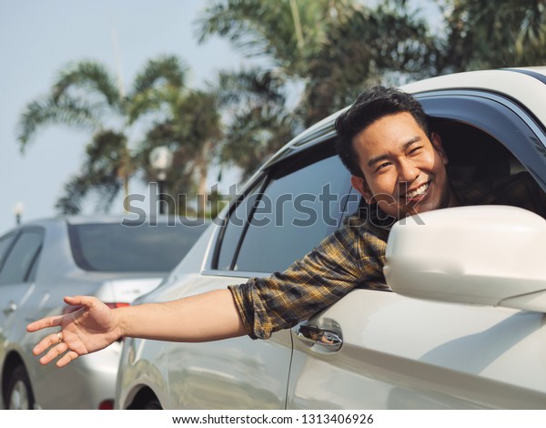 Happy Asian man in car raising hand out with\
city background.