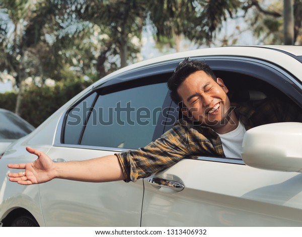 Happy Asian man in car raising hand out with\
city background.