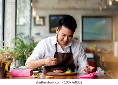 Happy Asian Man Decorating Valentine Cookies At Home, Lifestyle Concept.