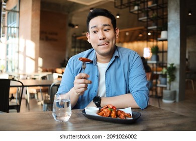 Happy  Asian Man Eating BBQ Chicken Wings In Restaurant.