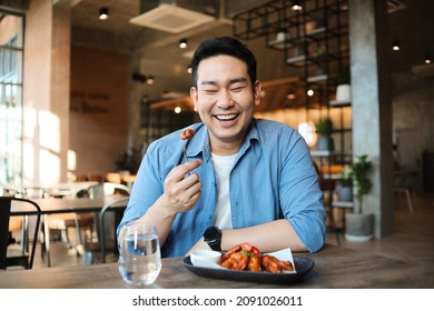 Happy  Asian man eating BBQ chicken wings in restaurant. - Shutterstock ID 2091026011